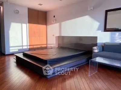 Modern bedroom with sleek platform bed and wooden flooring, bathed in natural light.