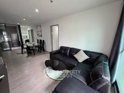 Modern living room with sleek black sectional sofa and dining area in open layout apartment.
