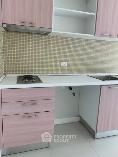 Modern kitchen with pink cabinets and mosaic backsplash, featuring a sleek electric stove and stainless steel sink.