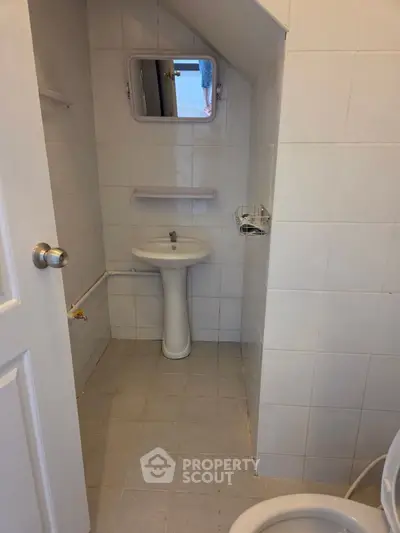 Compact bathroom with pedestal sink and wall-mounted mirror in a tiled space.
