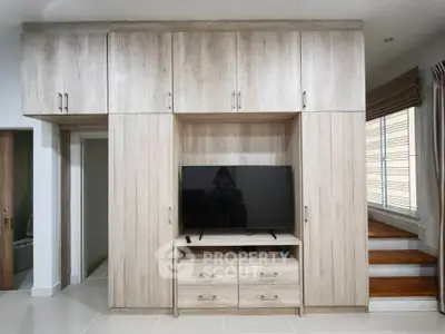 Modern living room with built-in wooden cabinets and TV, featuring sleek design and natural light.