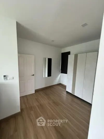 Spacious modern bedroom with sleek wooden flooring and ample storage space.