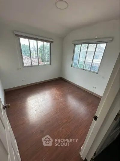 Spacious empty bedroom with wooden flooring and large windows offering natural light.