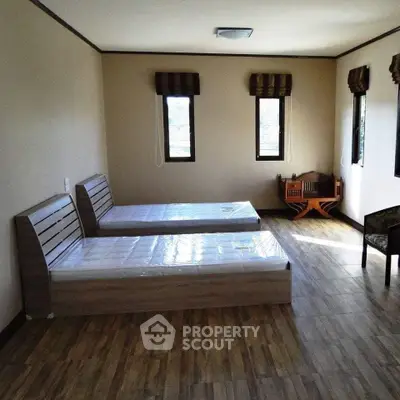 Spacious bedroom with twin beds and wooden flooring in a well-lit room.