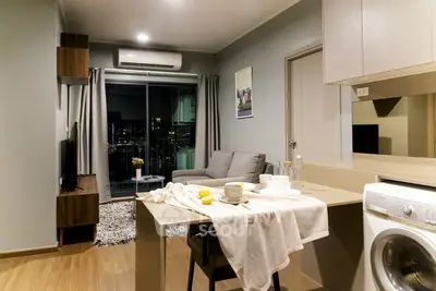 Modern living room with open kitchen and city view, featuring stylish decor and natural lighting.