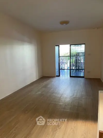 Spacious empty living room with wooden flooring and large windows leading to a balcony.