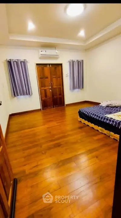 Spacious bedroom with wooden flooring and modern air conditioning