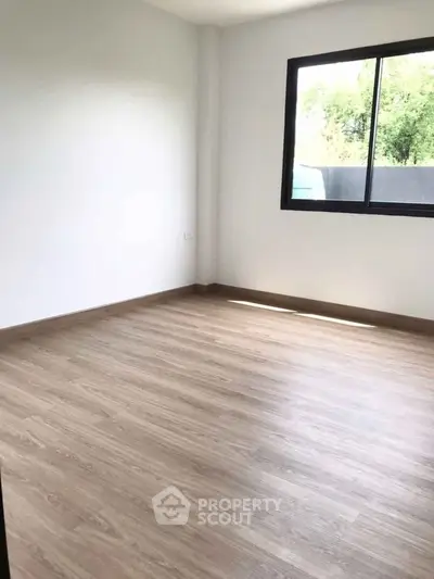 Spacious empty room with wooden flooring and large window, perfect for customization.