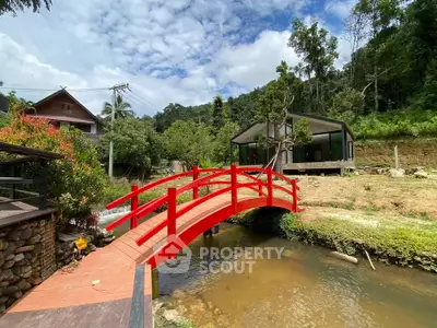 Charming countryside property with a red bridge over a stream and lush greenery.