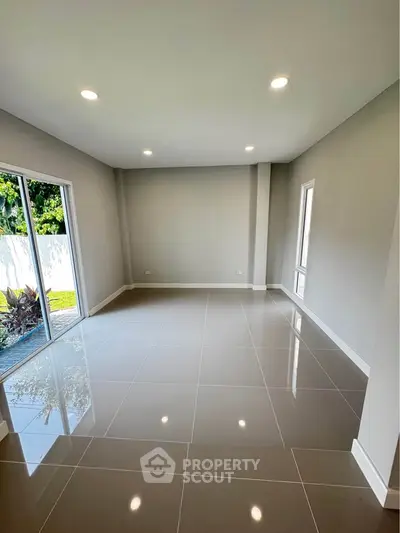 Spacious modern living room with large windows and glossy tiled floors, perfect for natural light.