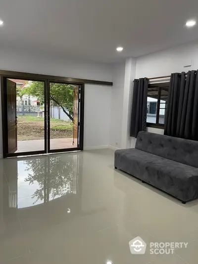 Spacious living room with modern sofa and large glass doors opening to garden view.