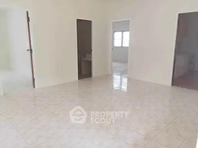 Spacious tiled room with multiple doorways and natural light, ideal for versatile living arrangements.