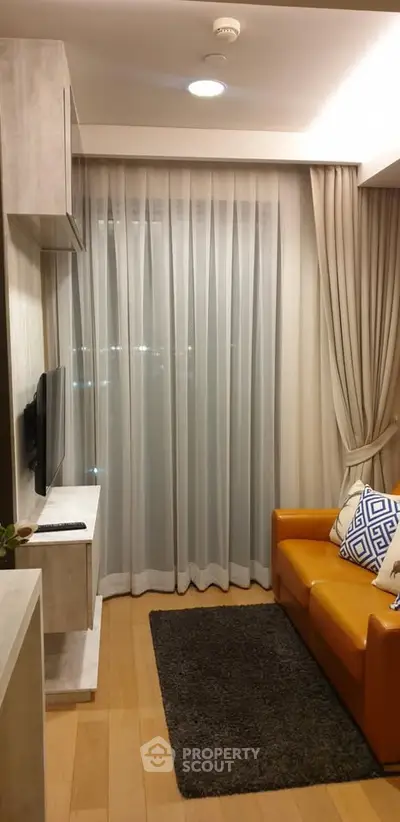 Cozy living room with modern decor and large window draped with sheer curtains.