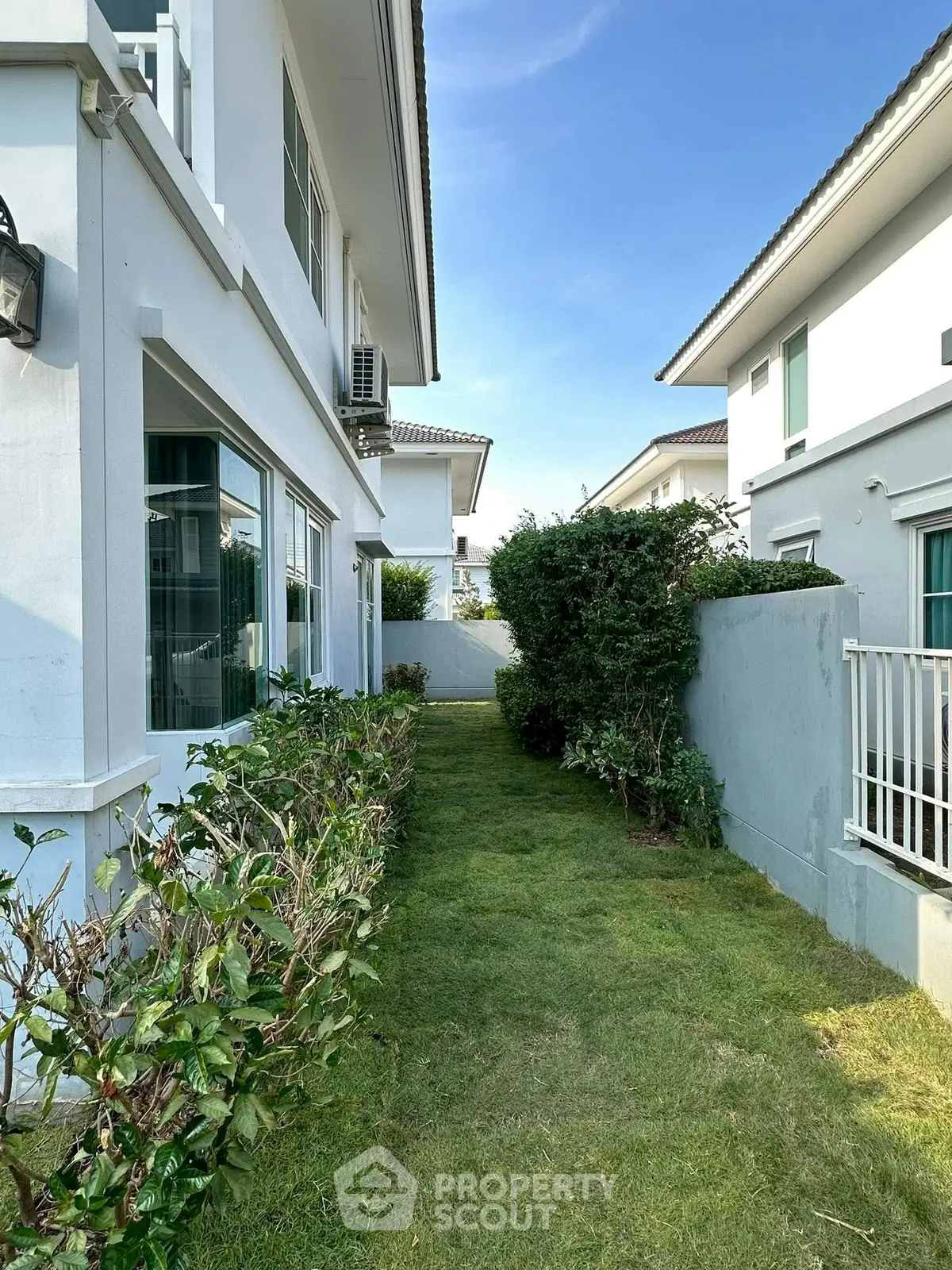 Charming side garden of a modern suburban home with lush greenery and white exterior walls.