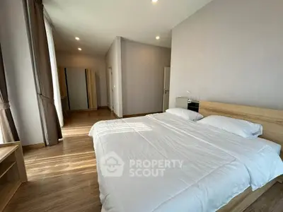 Spacious modern bedroom with wooden flooring and large windows for natural light.