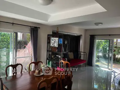 Spacious living room with dining area and garden view, featuring elegant wooden furniture and ample natural light.