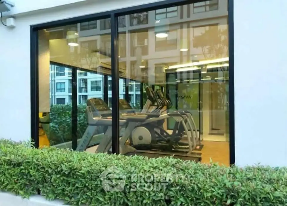 Modern gym with large windows in a residential building, featuring state-of-the-art exercise equipment.