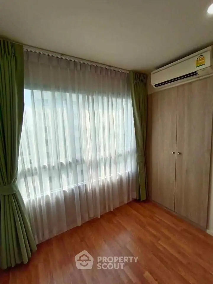 Bright bedroom with wooden flooring, green curtains, and built-in wardrobe.