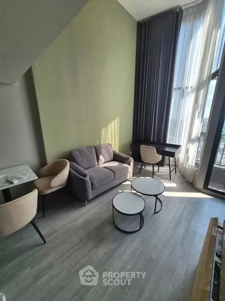Modern living room with high ceiling and large windows, featuring stylish furniture and abundant natural light.