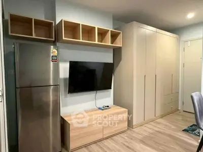 Modern living room with sleek storage, stainless steel fridge, and wall-mounted TV in stylish apartment.
