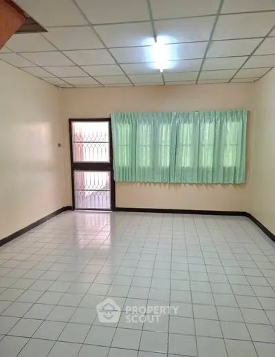 Spacious empty room with tiled floor and large window, perfect for customization.