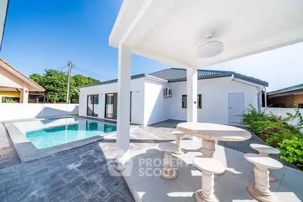 Modern white villa with pool and stylish outdoor seating area under blue sky.