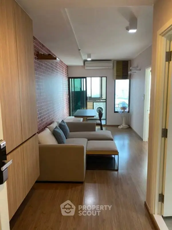Modern living room with stylish brick wall and cozy seating area, leading to a balcony with city view.