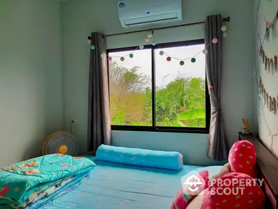 Cozy bedroom with vibrant blue flooring, large window offering lush green views, and playful decor, perfect for a restful retreat.