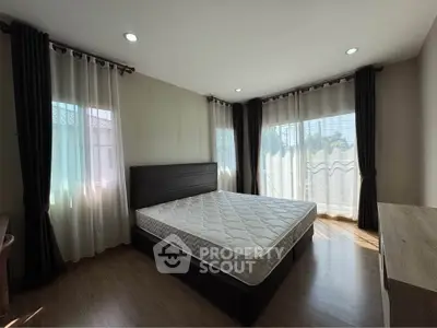 Spacious bedroom with large windows and natural light, featuring a comfortable bed and elegant curtains.
