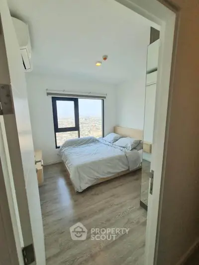 Bright bedroom with large window offering stunning city view, modern furnishings, and wooden flooring.