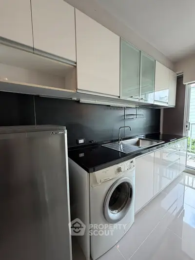 Modern kitchen with sleek cabinets, washing machine, and stainless steel fridge in a bright apartment.