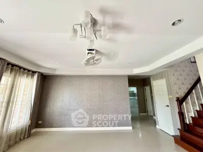 Spacious living room with elegant wallpaper and modern lighting, featuring a staircase and large windows.