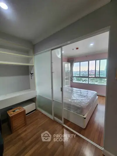 Modern bedroom with large windows and wooden flooring, featuring a cozy bed and built-in shelves.