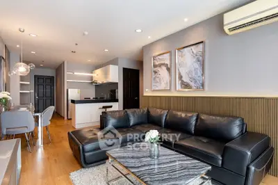 Modern living room with sleek black leather sofa and stylish kitchen in open layout.