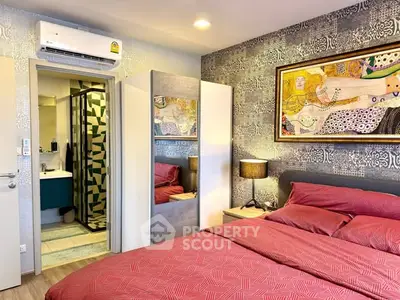 Stylish bedroom with modern decor and ensuite bathroom, featuring vibrant red bedding and artistic wall art.