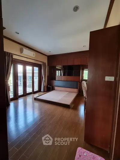 Spacious bedroom with wooden flooring and large windows for natural light.