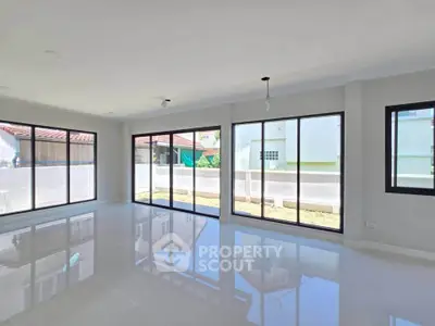 Spacious modern living room with large windows and glossy floors, offering abundant natural light and garden view.