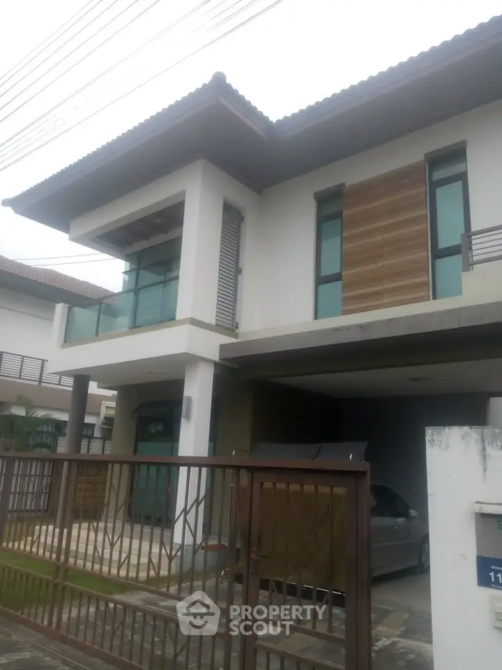 Modern two-story house with balcony and carport in a suburban neighborhood.