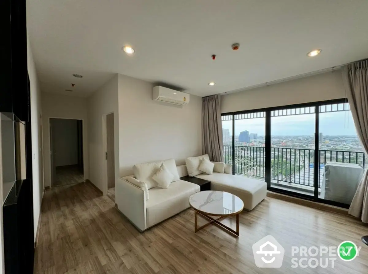 Modern living room with large windows and city view, featuring stylish furniture and wooden flooring.