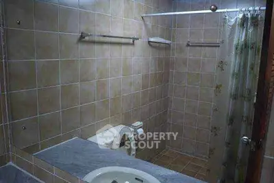 Cozy bathroom with tiled walls and shower curtain, featuring a sink and toilet.