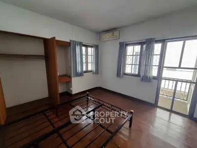 Spacious bedroom with wooden flooring and balcony access in a modern apartment.