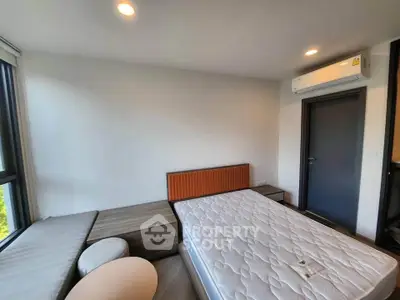 Modern bedroom with natural light, featuring a large window, air conditioning, and minimalist furniture.
