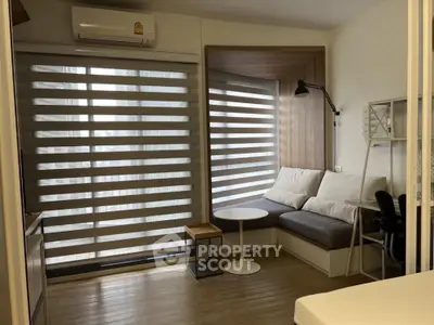 Modern cozy living room with natural light filtering through wooden blinds, featuring a comfortable L-shaped sofa, sleek furniture, and warm wooden flooring.