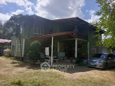 Charming green two-story home with spacious covered porch and lush surroundings, perfect for tranquil living.