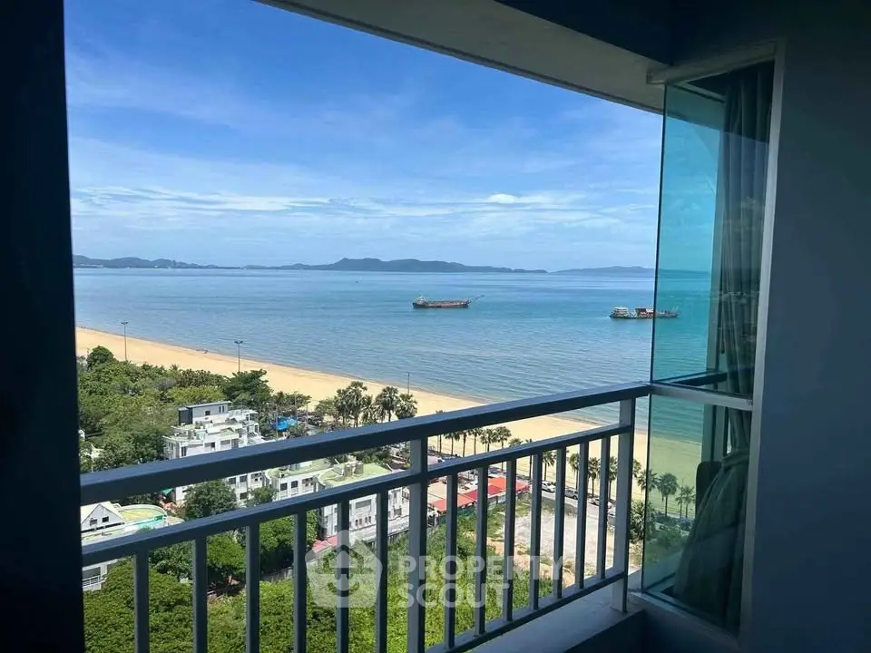 Stunning ocean view from a high-rise balcony overlooking a sandy beach and clear blue waters.
