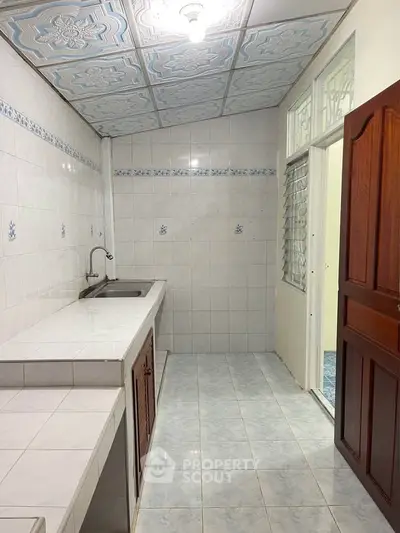 Spacious kitchen with tiled walls and ceiling, featuring a single sink and wooden cabinetry.