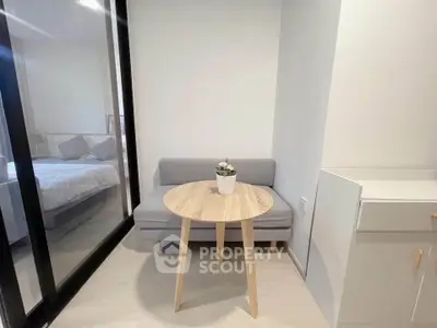 Cozy small living area with modern sofa and round table, adjacent to a bedroom with glass partition.