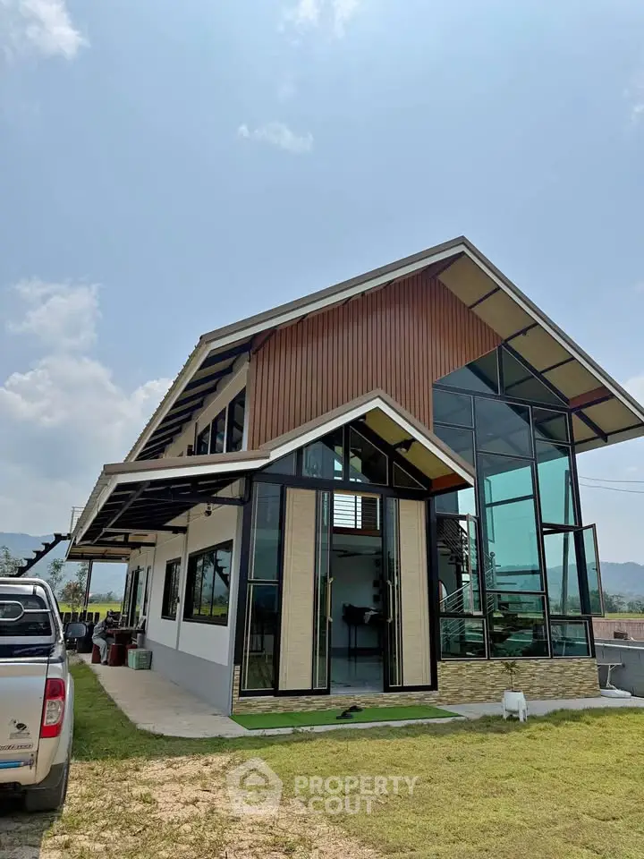 Modern architectural house with large glass windows and sloped roof, set against a clear sky and mountain backdrop.
