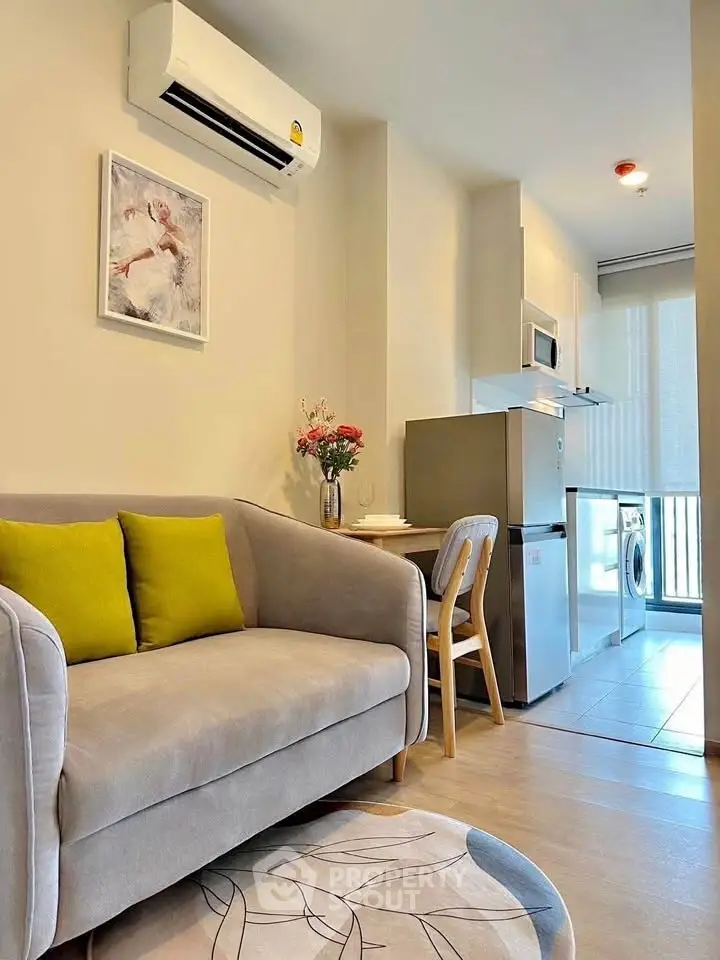 Modern living room with cozy sofa, air conditioning, and compact kitchen area featuring fridge and washing machine.