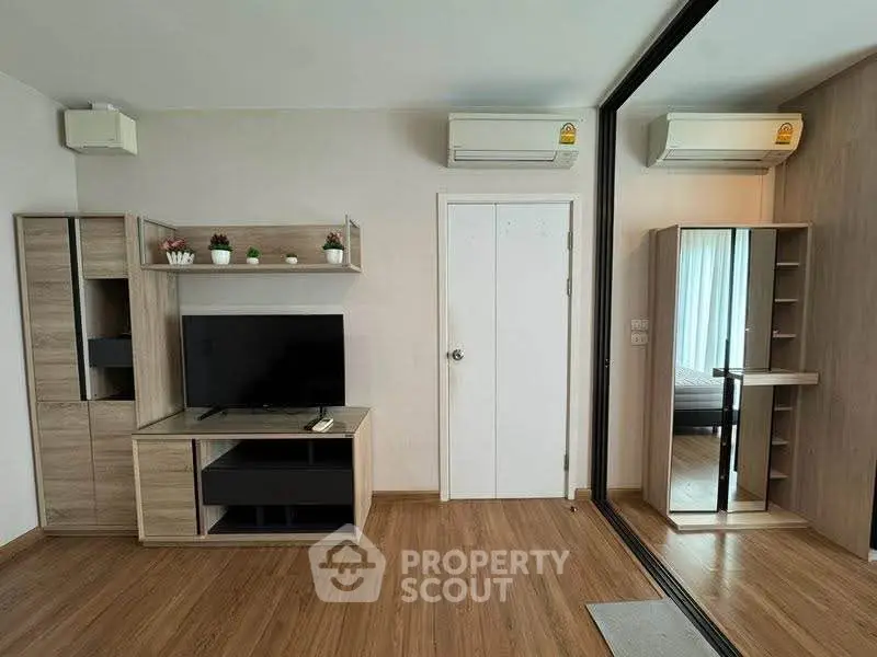 Modern living room with wooden flooring, TV unit, and mirrored wardrobe in stylish apartment.
